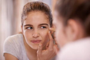 A teenage girl looking inn the mirror squeezing a pimple