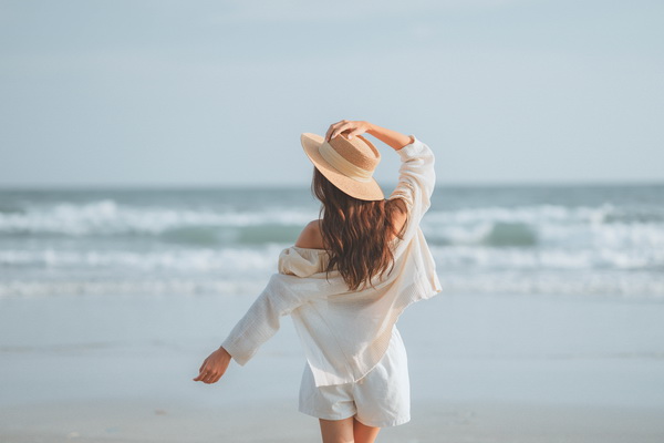 Woman with long brown hair wearing a sun hat at the beach, protecting hair from summer heat and UV rays