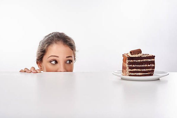 Shot of a young woman sneak up to a piece of cke standing on a table