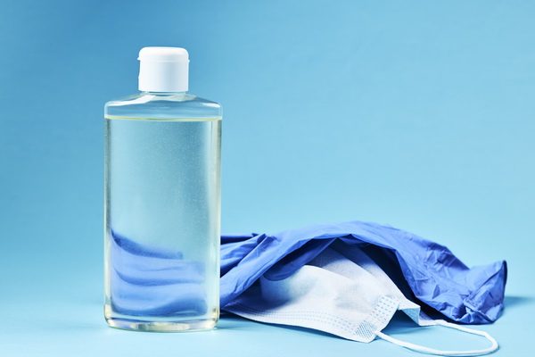 blank hand sanitizer with face mask and latex gloves over blue background. copy space. covid-19 symbol concept.
