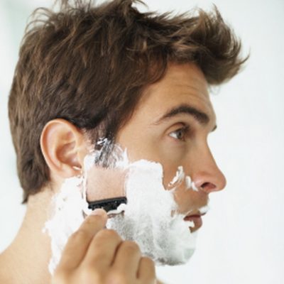 dark haired man shaving in a mirror
